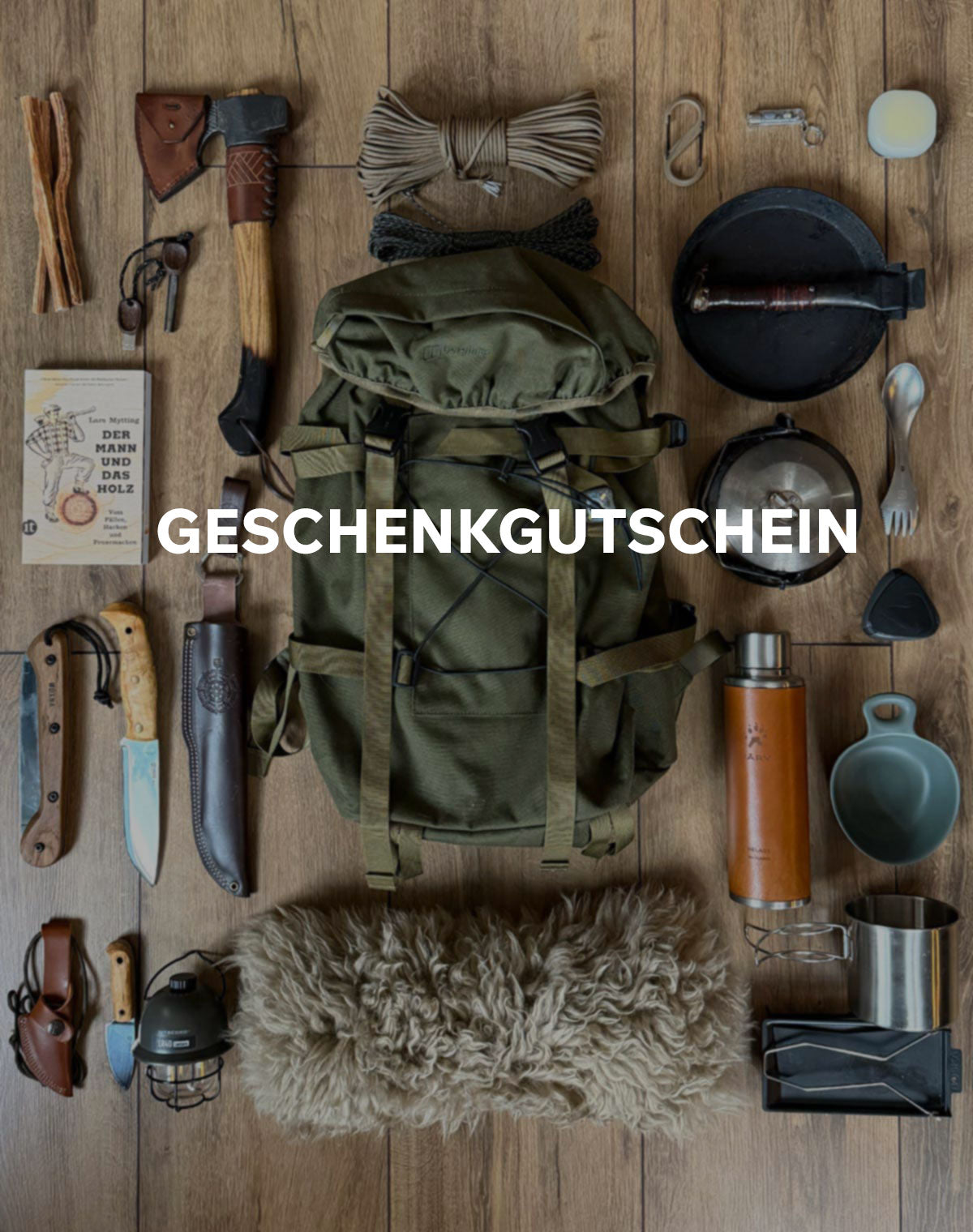 Geschenkgutschein von Fritz und Frei, umgeben von Outdoor-Ausrüstung mit Messern, Rucksack, Merinofell und Campingkocher