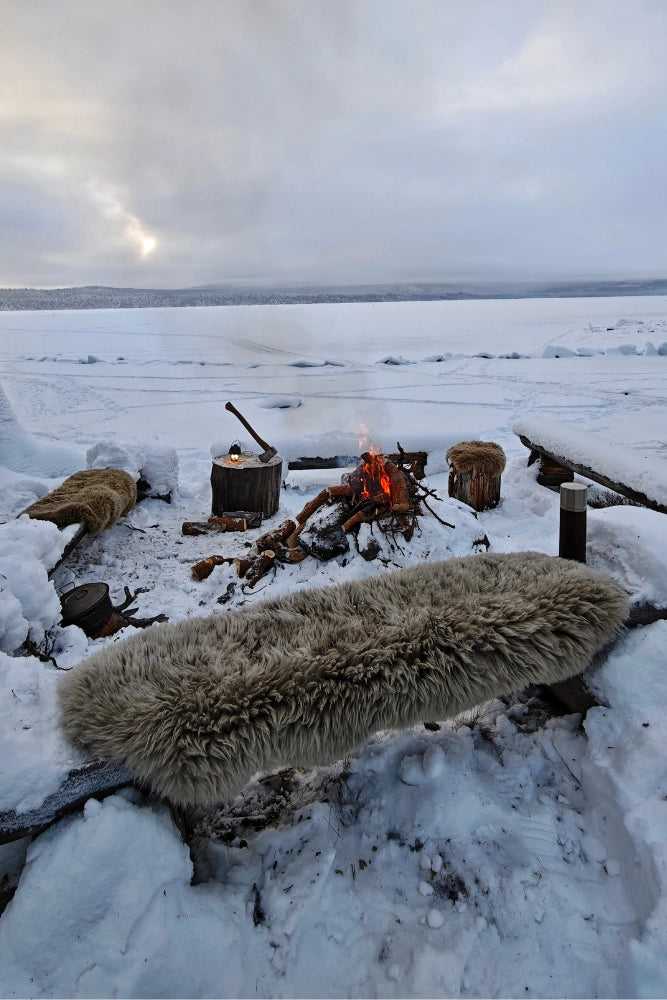 Fritz und Frei Schaffell Sitzauflage aus Australien auf Holzbank beim Wintercamping vor dem Lagerfeuer