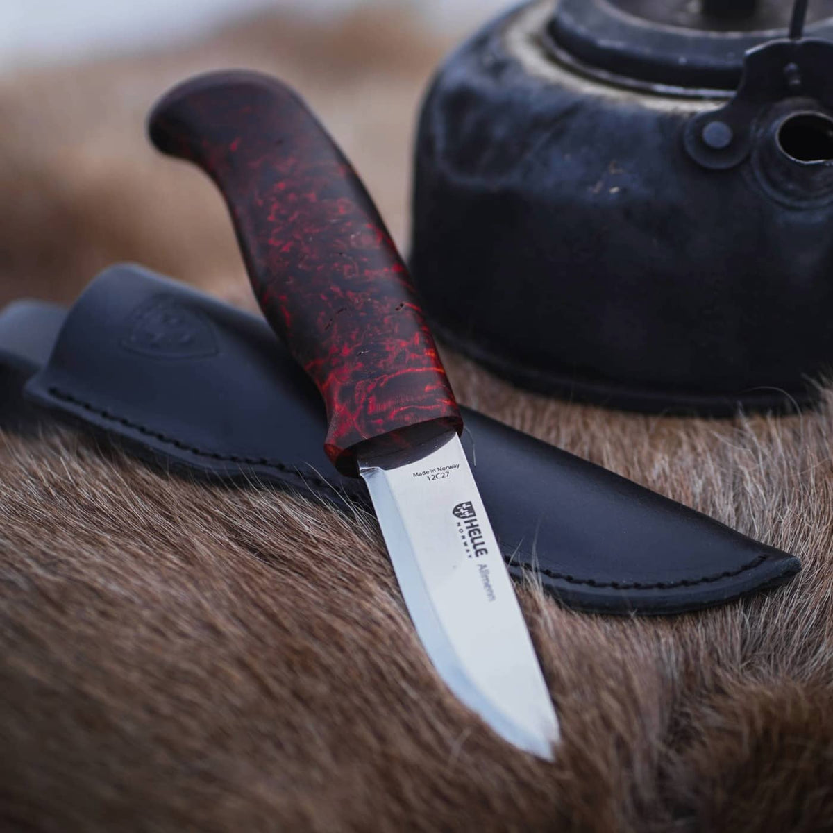 Helle Allmenn Outdoor-Messer mit schwarzer Lederscheide auf einem Fell liegend
