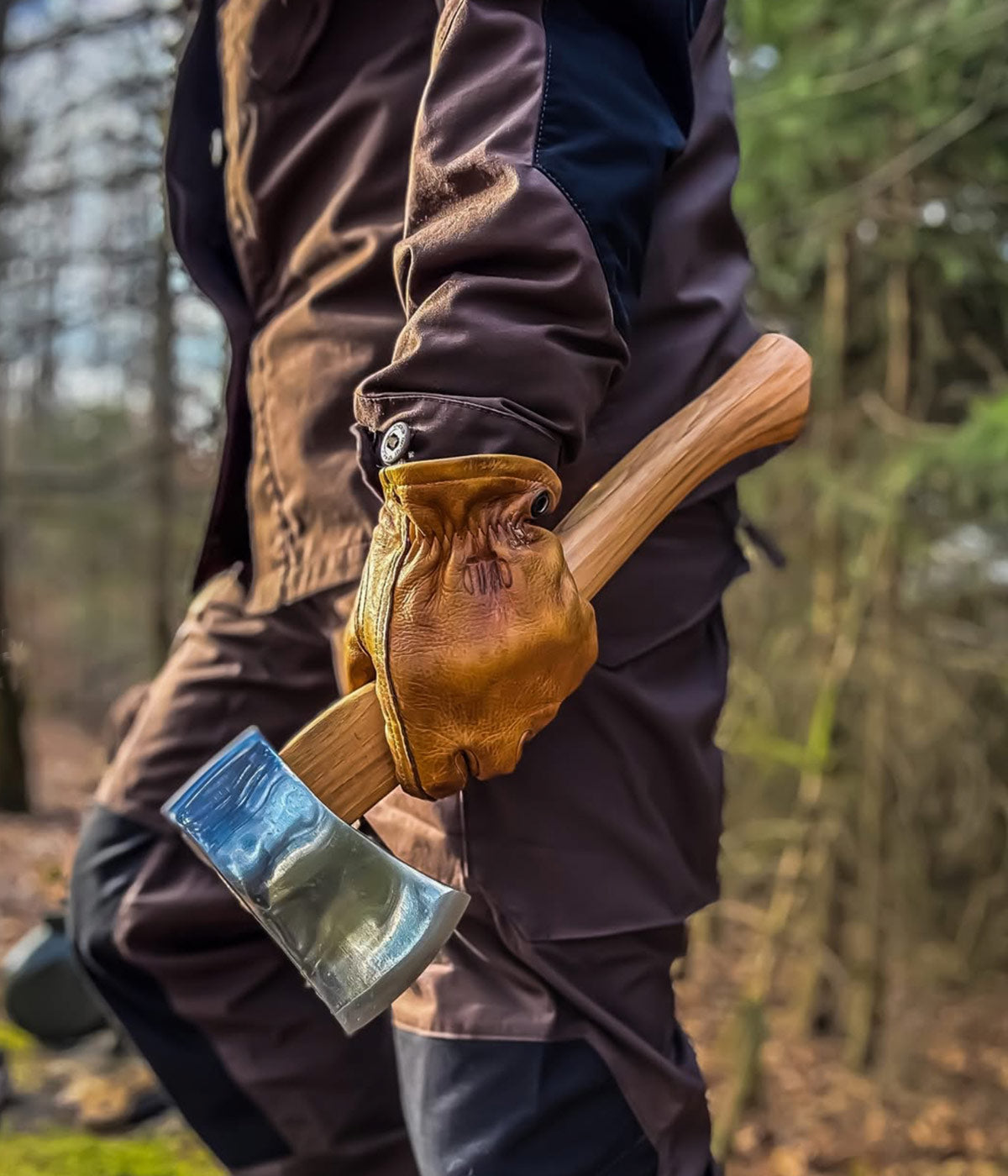 Behandschuhte Hand hält ein Helko Werk Pfadfinderbeil mit Hickorystiel und poliertem Kopf im Wald