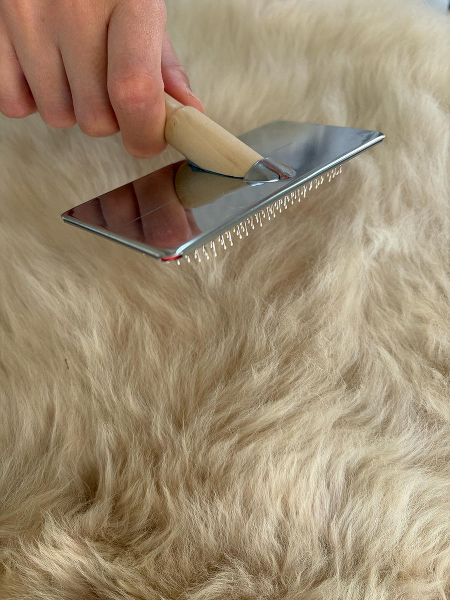 Fellbuerste mit Holzgriff wird durch die Wolle eines Merino Schaffells gezogen