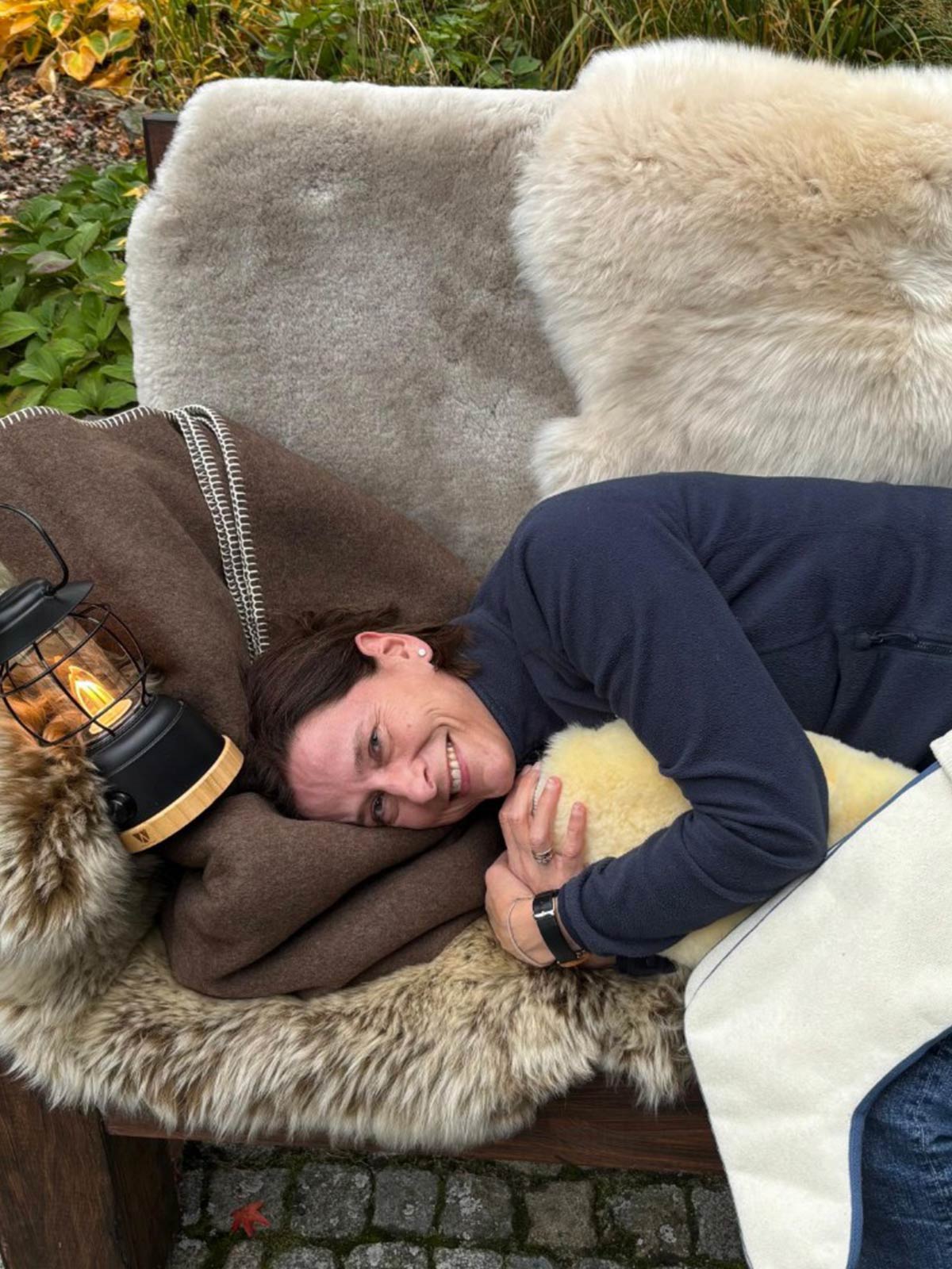 Merino Schaffell auf einer Holzbank draußen im Herbst, daneben eine Laterne