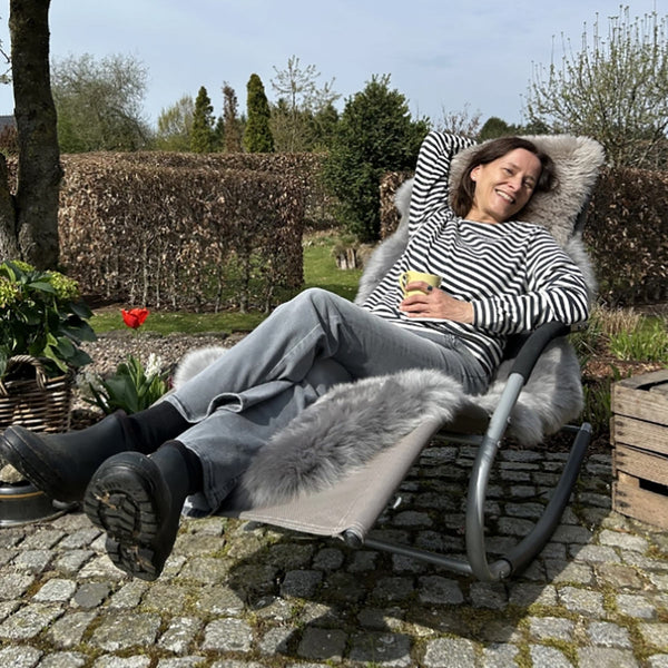 Frau entspannt auf einem Liegestuhl mit Merino Schaffell im Garten