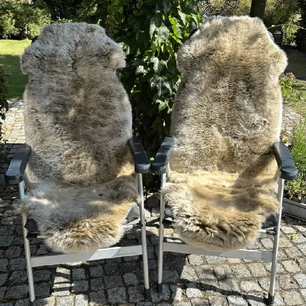 Zwei Campingstuehle mit grauen Merino Schaffellen als Auflage in einem Garten