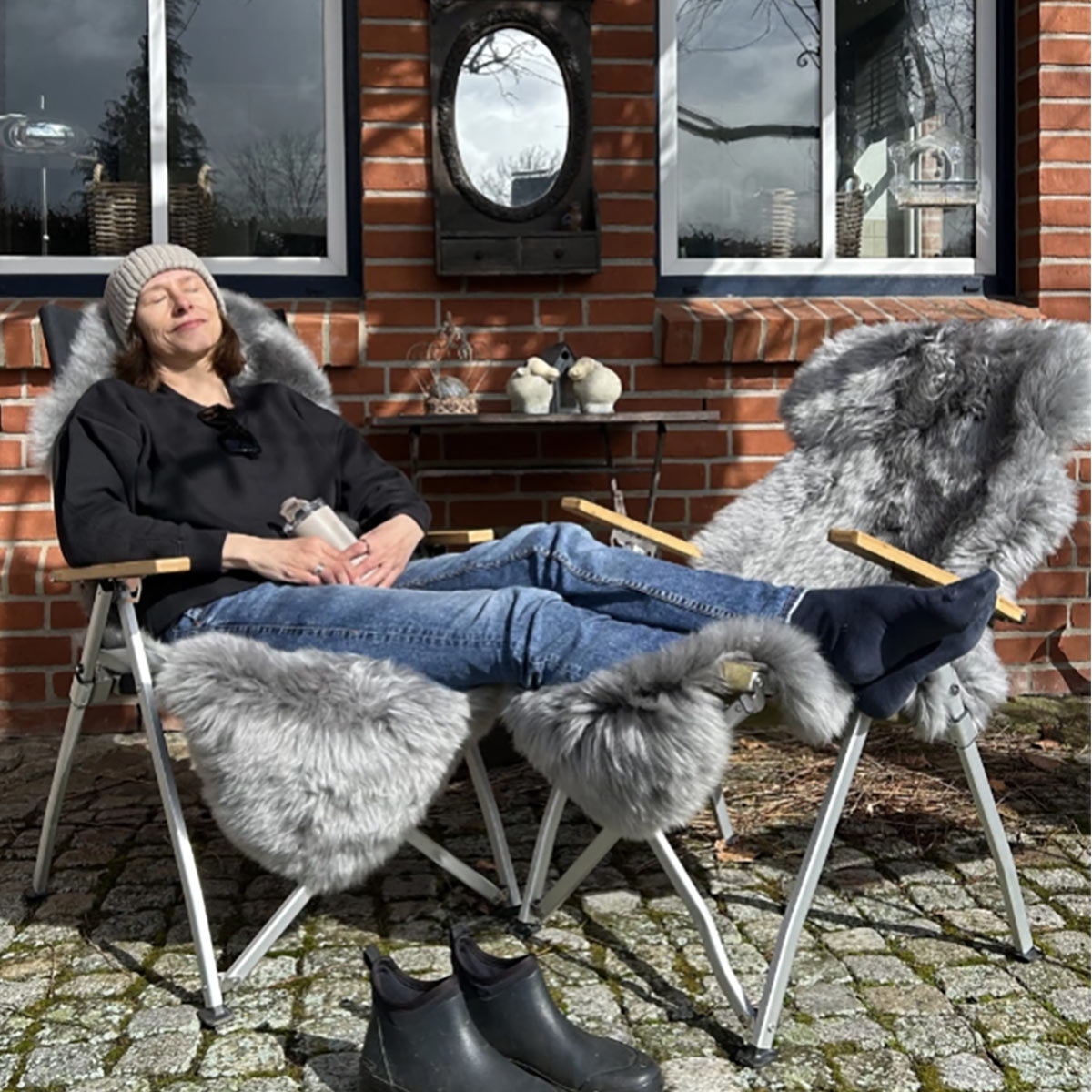 Zwei Campingstühle mit grauen Merino Schaffellen auf einer Terrasse, Frau sitzt entspannt darin